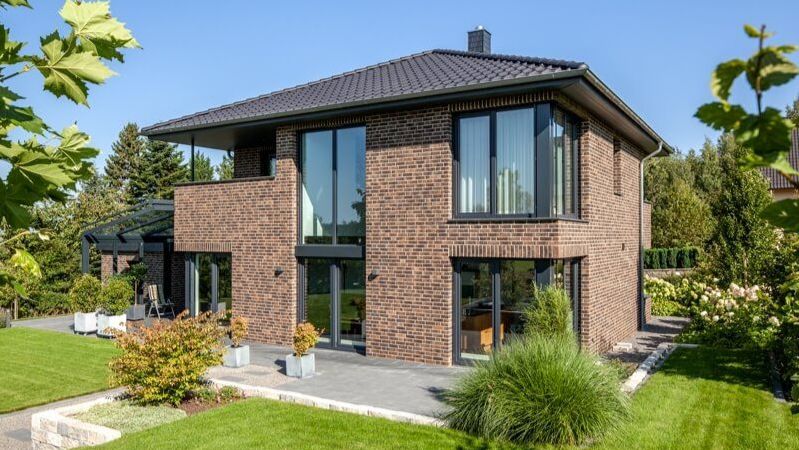 The hipped roof with a shallow pitch and beautiful overhangs is robust and practical. Large windows, and some in the corner of the house, illuminate the interior space well and accentuate the modern style of this brick-finished aerated concrete house.
