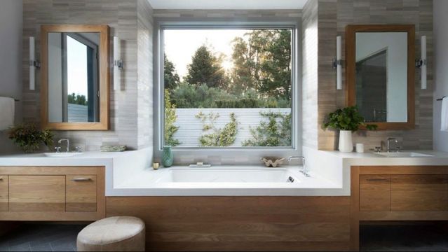 Современная ванная комната с деревянными шкафами и серой керамической плиткой. 